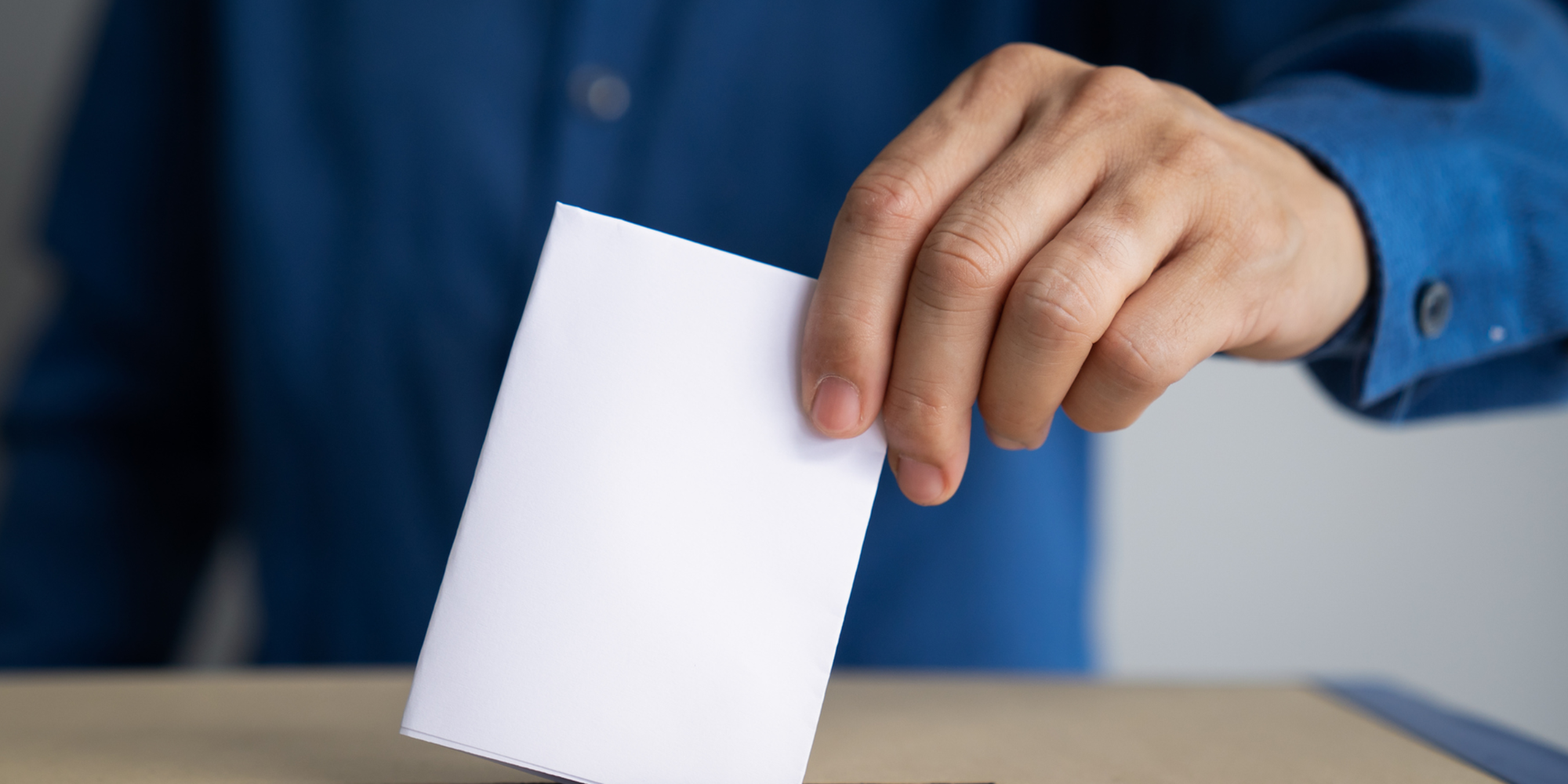 Eine Hand wirft einen gefalteten Stimmzettel in eine weisse Wahlurne