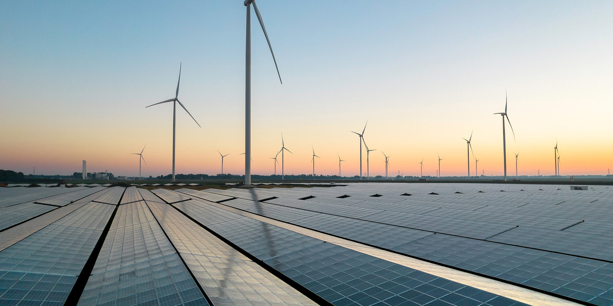 Reflected sky on a solar panel field during a summer sunrise. Wind turbines can be seen on the horizon.Muntendam, the Netherlands, September 2023