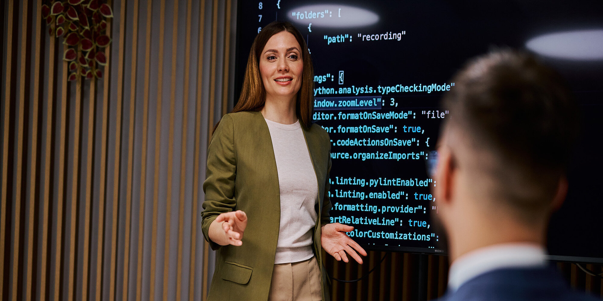Female software developer is presenting code on a monitor to her colleague during a business meeting, discussing programming and development strategies