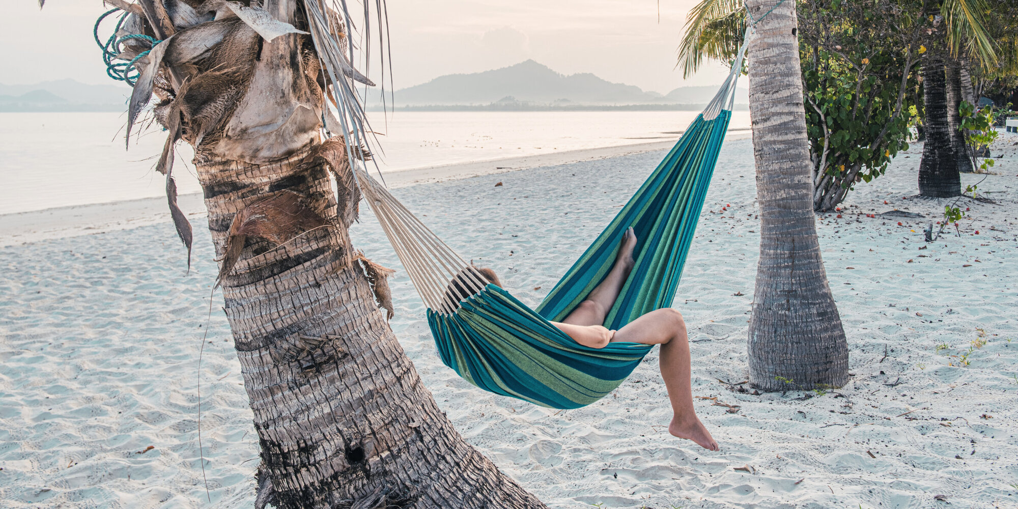 Touristin, die an einem Palmenstrand in einer Hängematte liegt