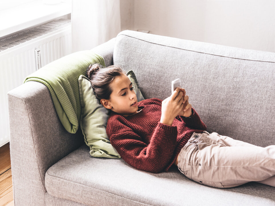 Auf dem Sofa liegendes Mädchen, das sein Handy in der Hand hat