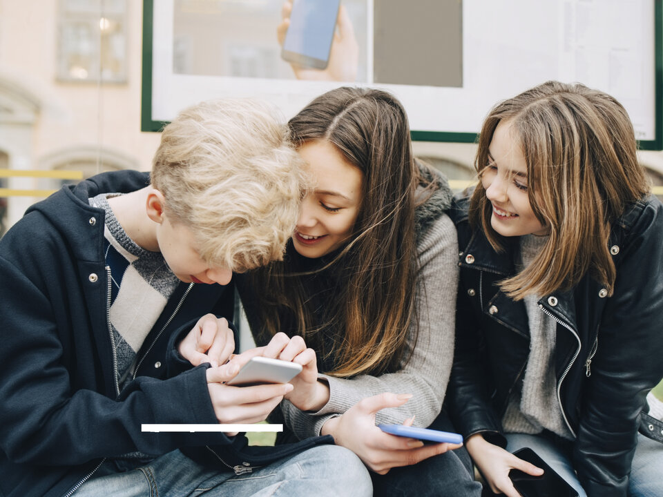 Lächelnde Teenager die sich über ein Smartphone beugen