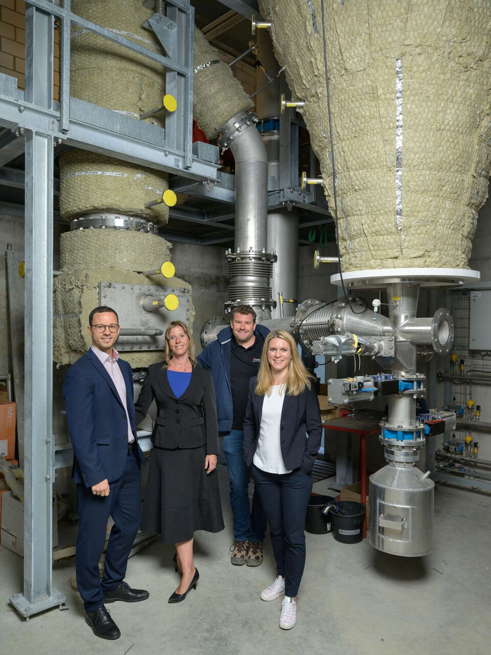 Stippvisite auf dem Hof: (v.l.n.r.) Kundenberater Stefan Häusler, Tamara Götz-Graf, Produktmanagerin Umweltdarlehen und Marit Kruthoff, Fachbeauftragte Leistungsaufrag und zuständig für den Nachhaltigkeitsauftrag, besuchten im vergangenen Jahr Landwirt Florian Gut (3. von links), den stolzen Besitzer der pionierhaften Holzenergie-Anlage im Hintergrund. (Bild: Stefan Walter)