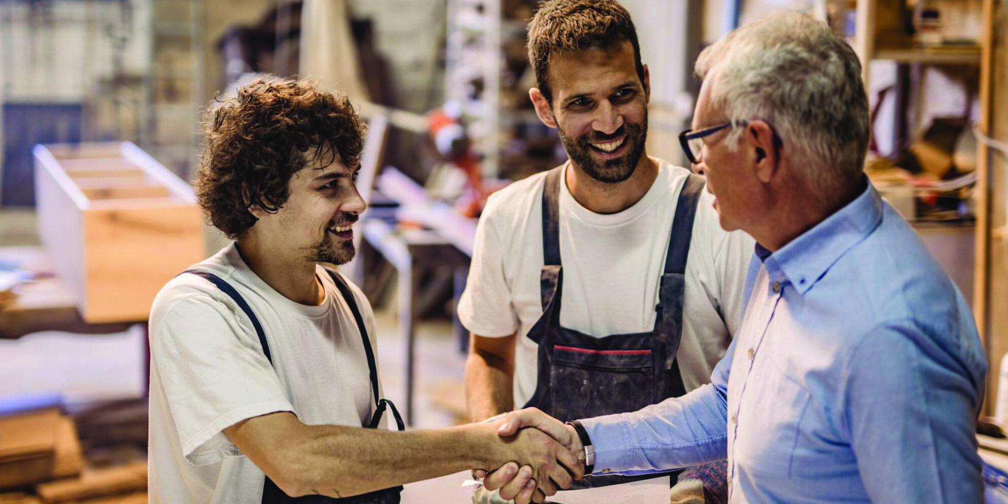 Zwei Schreiner und ein Kunde, die sich in der Werkstatt die Hände schütteln