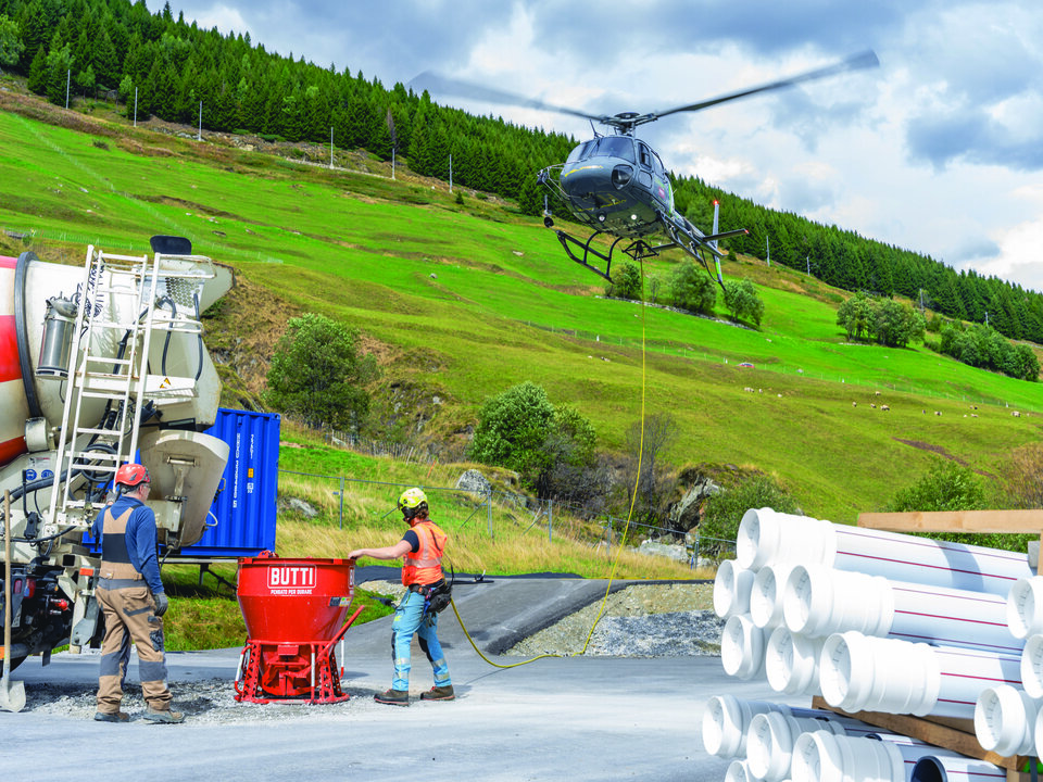 Ein Helikopter holt im Tal eine Ladung Beton für den Transport zur Baustelle oberhalb von Sedrun.